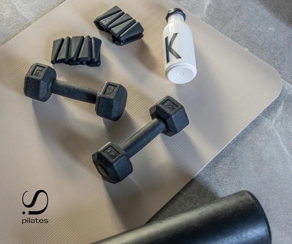 Pilates equipment on a mat – dumbbells, ankle weights and a water bottle